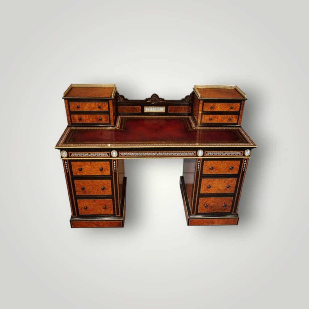 A Victorian ebonised and thuya wood pedestal desk featuring a leather writing surface, raised side drawers, ivory inlay, and ceramic plaque details.
