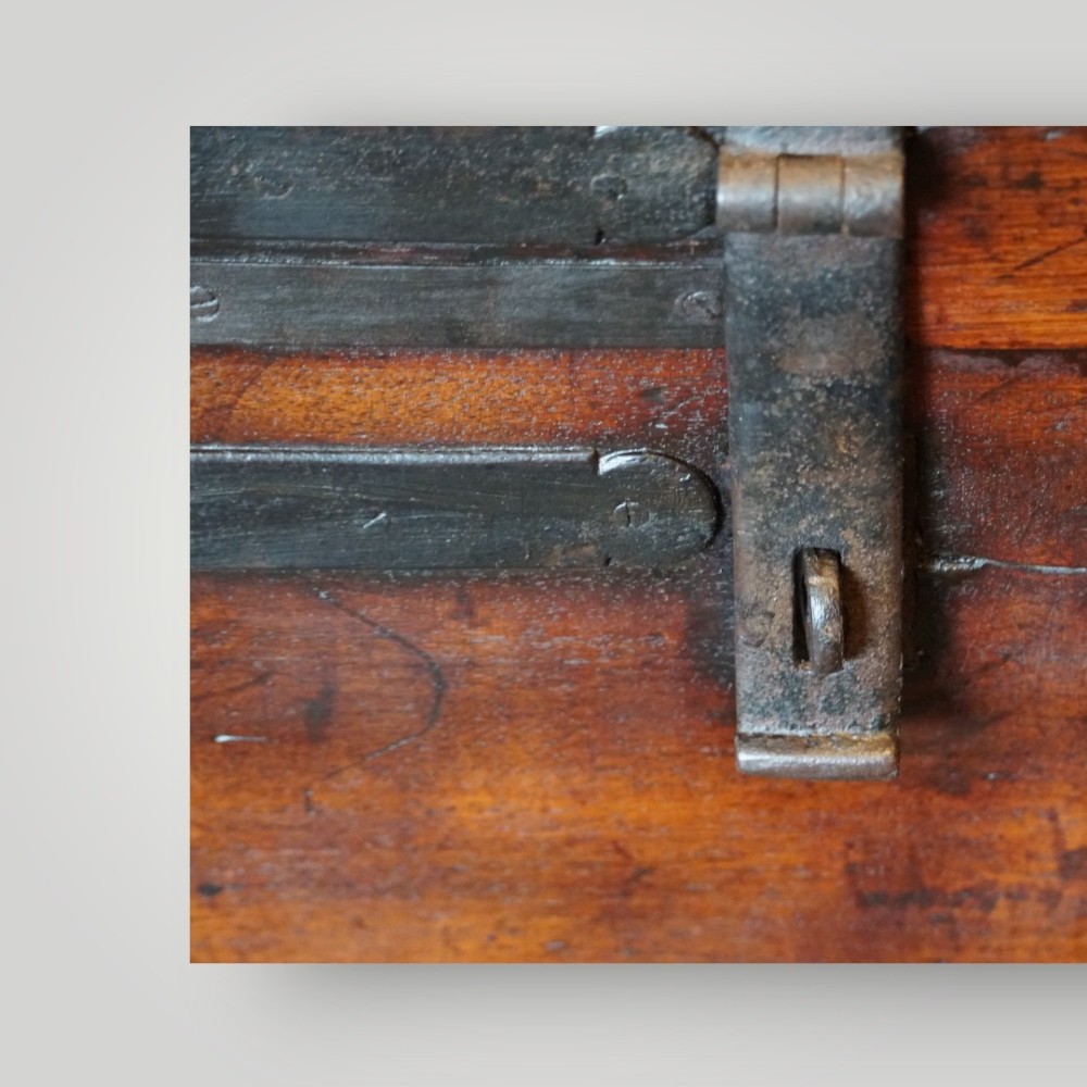 A rectangular antique walnut wood trunk featuring heavy iron binding straps, metal corner hardware, and a brass plaque on the lid. View VI