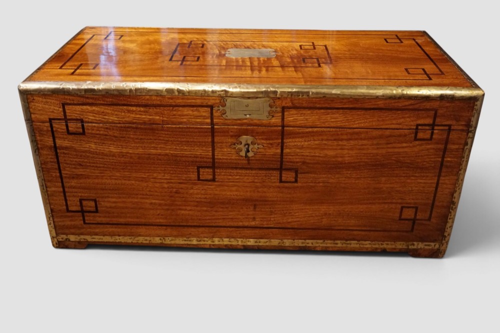 A rectangular Victorian camphor wood campaign chest featuring polished brass binding along the edges, geometric dark line inlay, and a central brass lock escutcheon. View VII