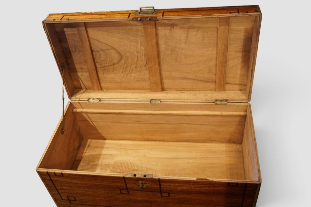 A rectangular Victorian camphor wood campaign chest featuring polished brass binding along the edges, geometric dark line inlay, and a central brass lock escutcheon. View IX