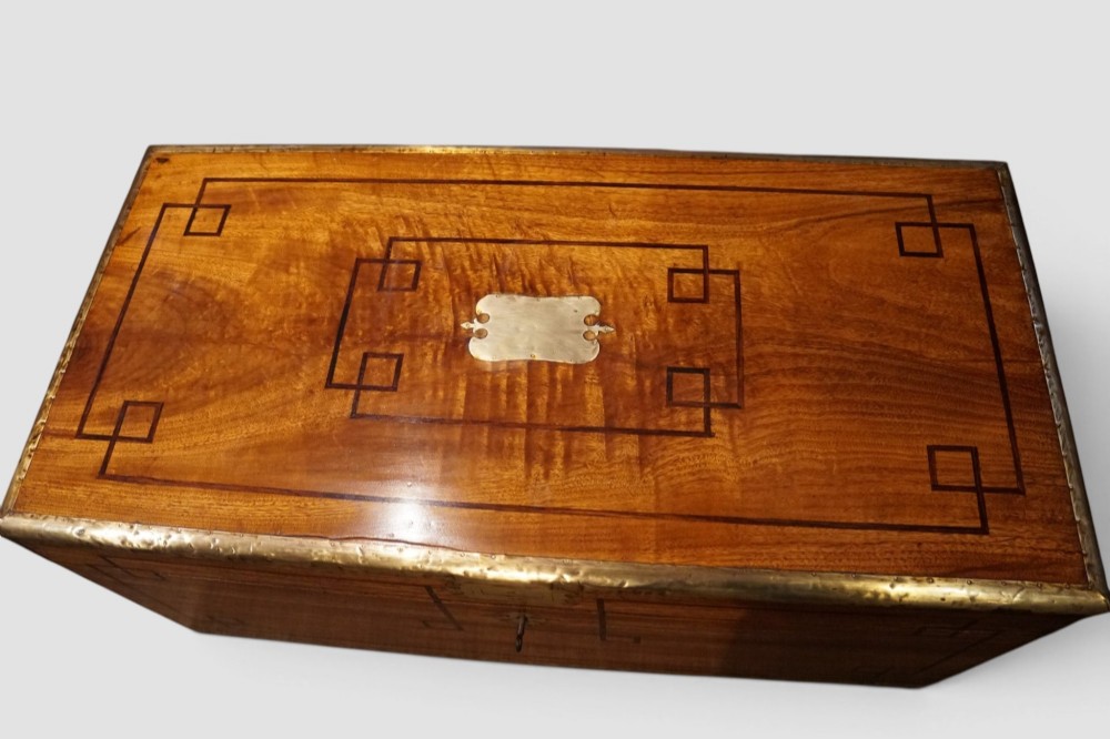 A rectangular Victorian camphor wood campaign chest featuring polished brass binding along the edges, geometric dark line inlay, and a central brass lock escutcheon. View XI