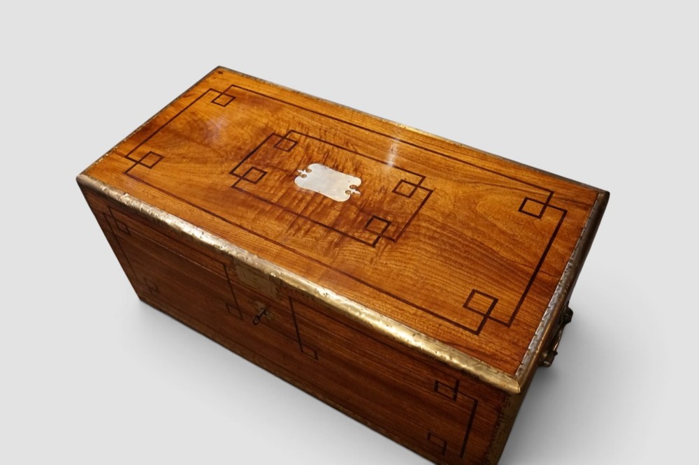 A rectangular Victorian camphor wood campaign chest featuring polished brass binding along the edges, geometric dark line inlay, and a central brass lock escutcheon. View XII