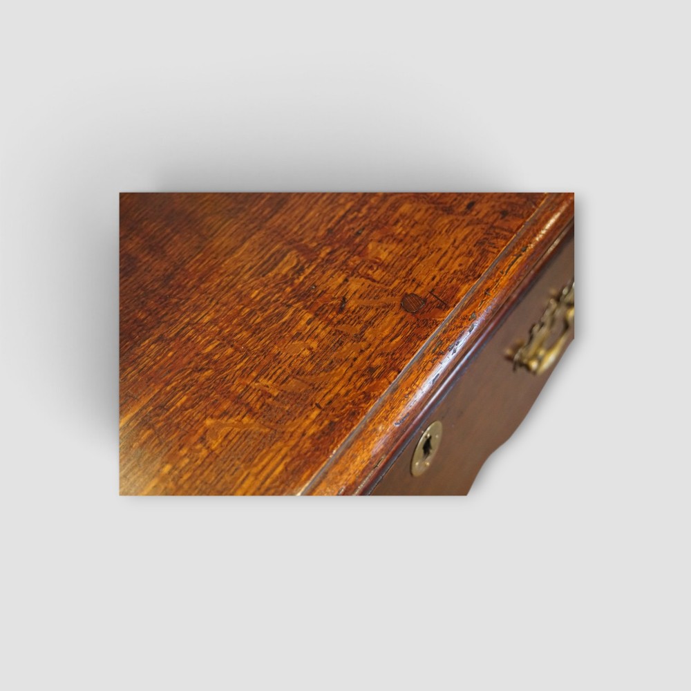 An 18th-century George III dark oak dresser base featuring three drawers with brass handles and a scalloped apron on turned legs. View V