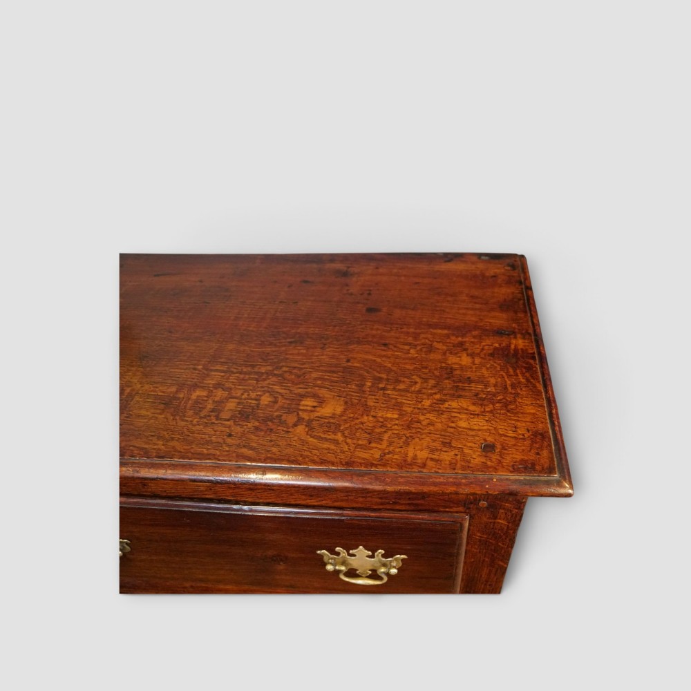 An 18th-century George III dark oak dresser base featuring three drawers with brass handles and a scalloped apron on turned legs. View XI