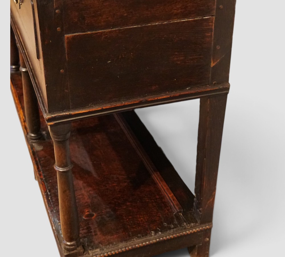 An antique dark oak dresser base featuring three frieze drawers with brass handles supported by turned legs and a low open potboard shelf. View V