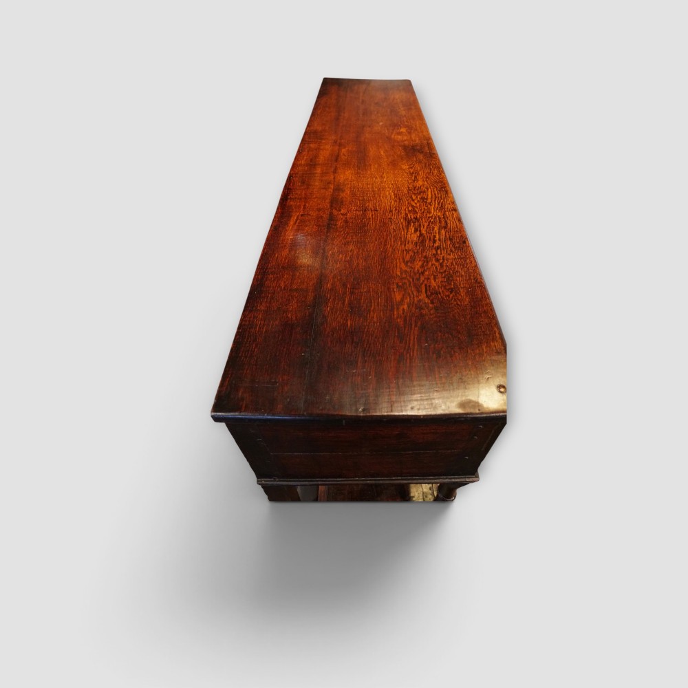 An antique dark oak dresser base featuring three frieze drawers with brass handles supported by turned legs and a low open potboard shelf. View VII