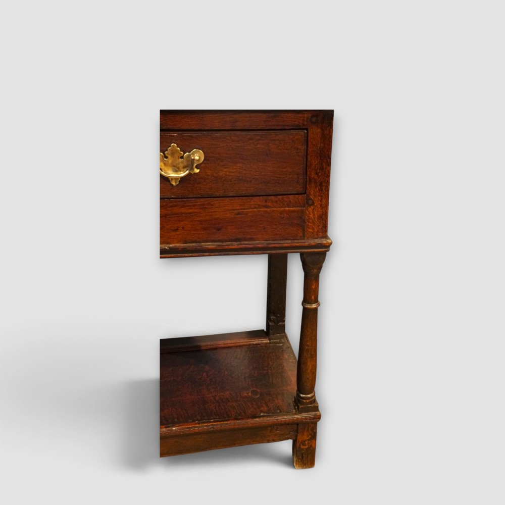 An antique dark oak dresser base featuring three frieze drawers with brass handles supported by turned legs and a low open potboard shelf. View VIII