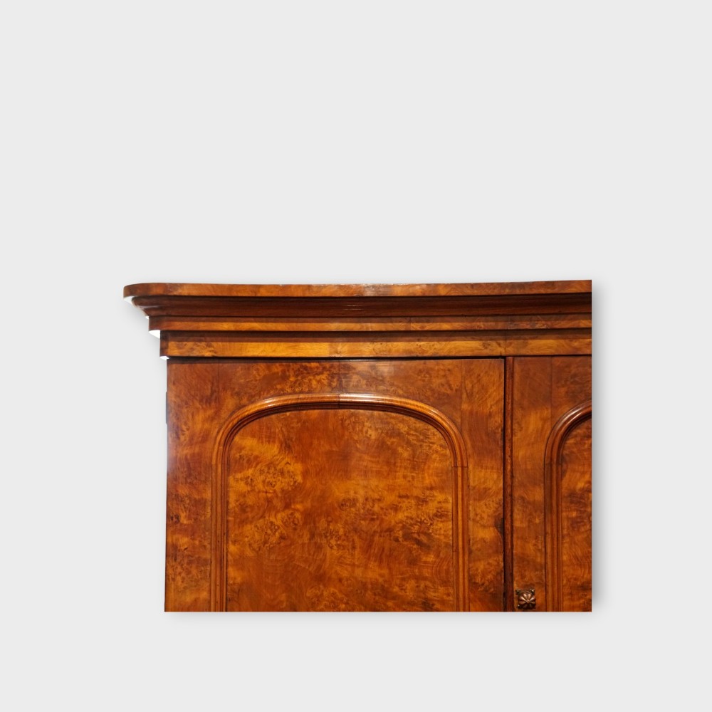 A 19th-century Victorian burr walnut linen press featuring an upper cabinet with arched panel doors over a chest of four drawers with turned wooden knobs. View IV