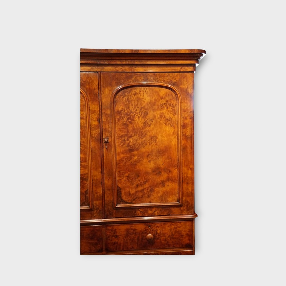 A 19th-century Victorian burr walnut linen press featuring an upper cabinet with arched panel doors over a chest of four drawers with turned wooden knobs. View V