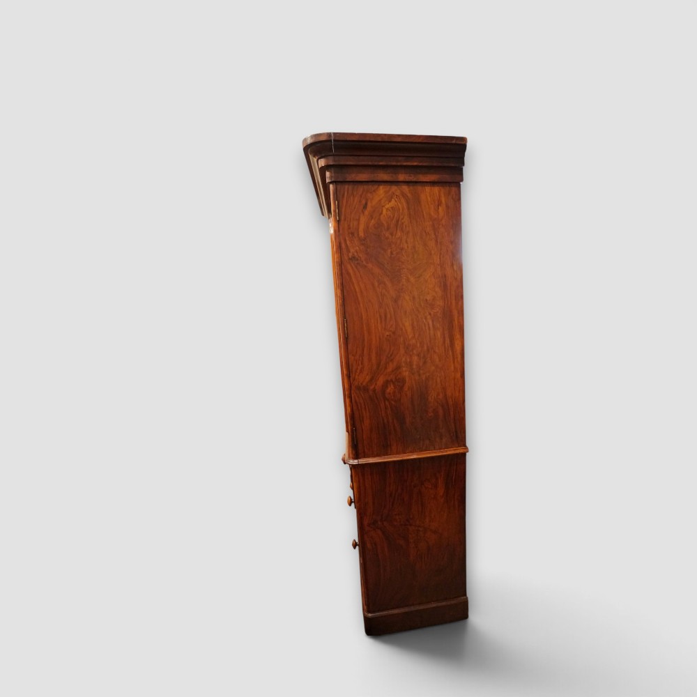 A 19th-century Victorian burr walnut linen press featuring an upper cabinet with arched panel doors over a chest of four drawers with turned wooden knobs. View X