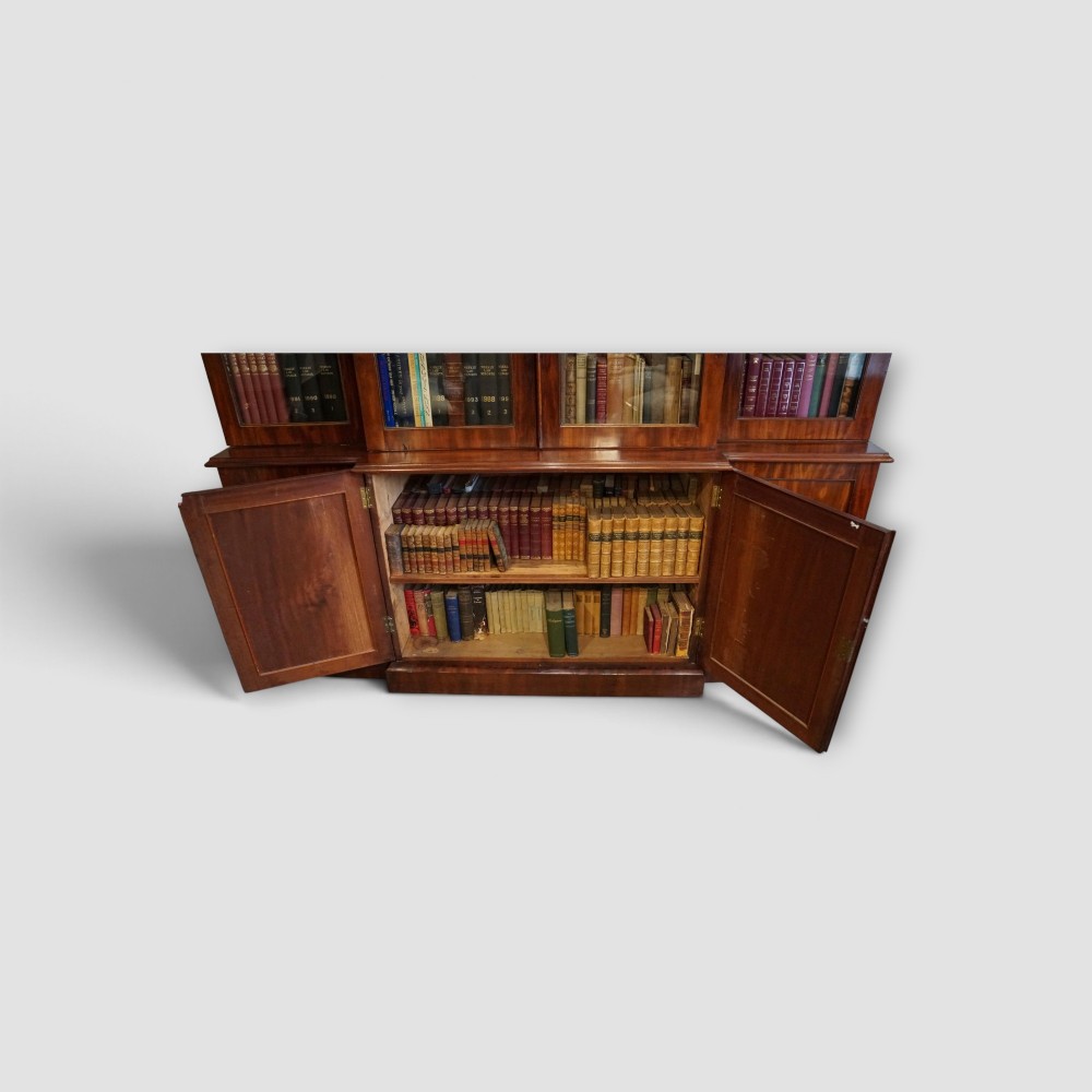 A 19th-century mahogany breakfront bookcase featuring glazed upper doors filled with books above solid panelled cupboard doors. View IV