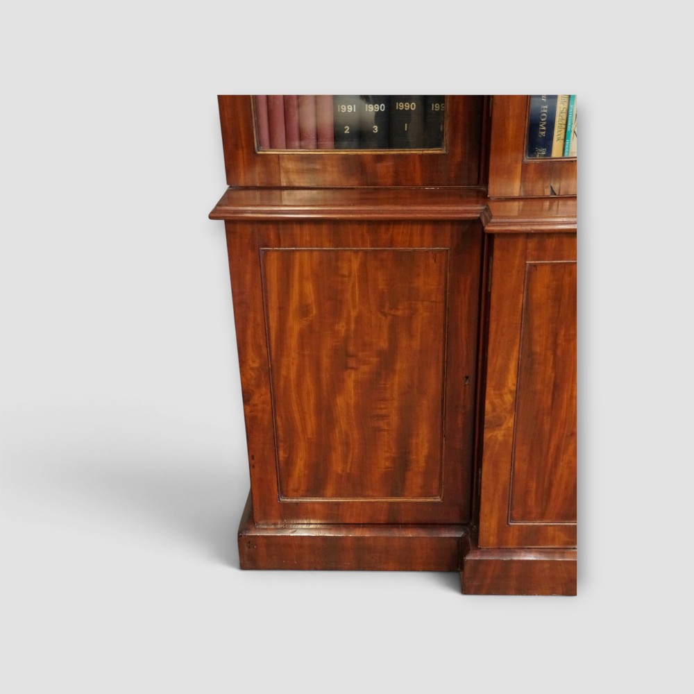 A 19th-century mahogany breakfront bookcase featuring glazed upper doors filled with books above solid panelled cupboard doors. View IX