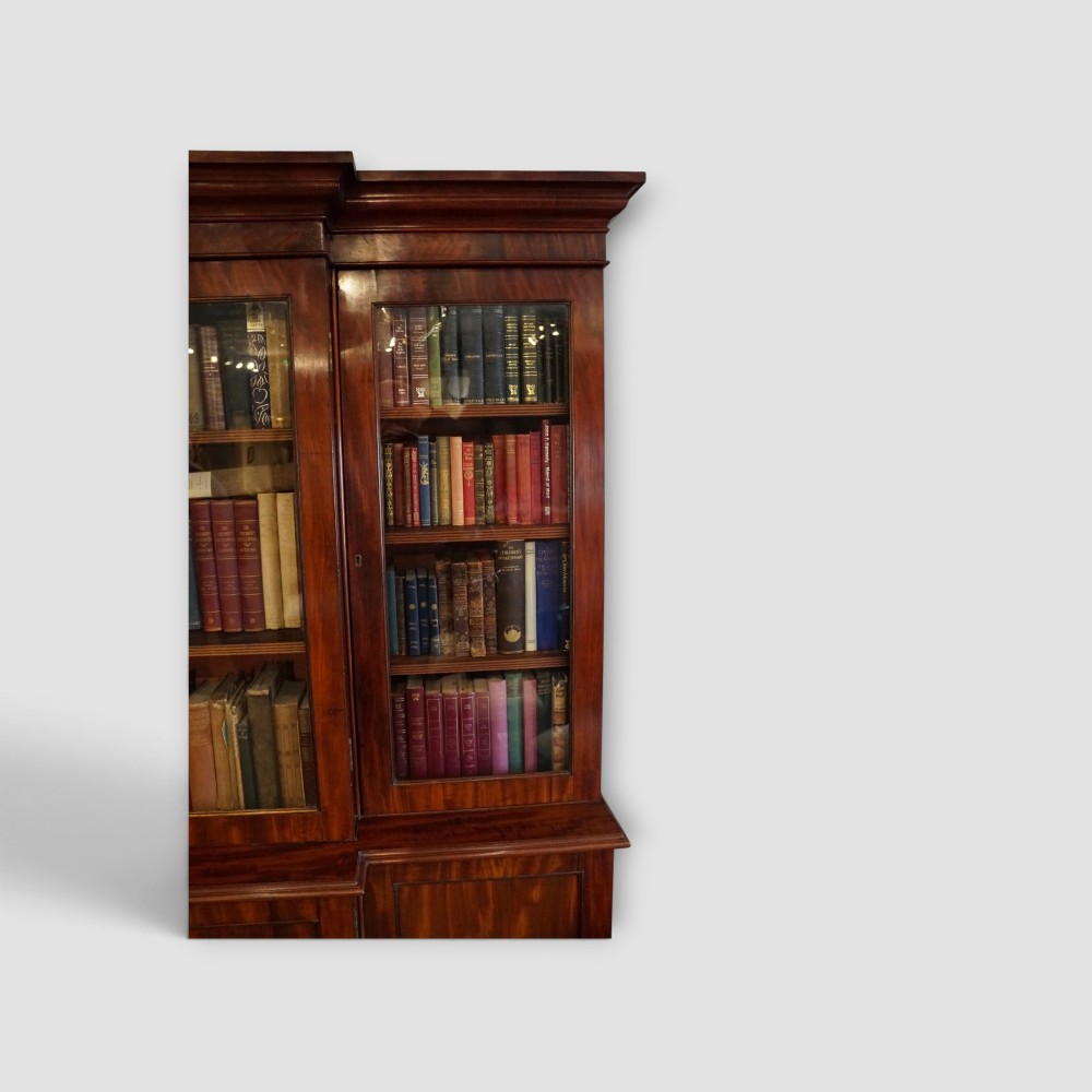 A 19th-century mahogany breakfront bookcase featuring glazed upper doors filled with books above solid panelled cupboard doors. View XI