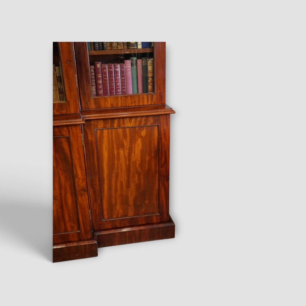 A 19th-century mahogany breakfront bookcase featuring glazed upper doors filled with books above solid panelled cupboard doors. View XII