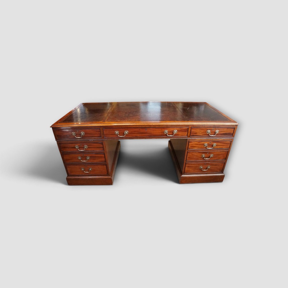 A large Victorian mahogany partners desk featuring a brown leather inset writing surface, twin drawer pedestals, brass swan-neck handles, and a wide central kneehole.