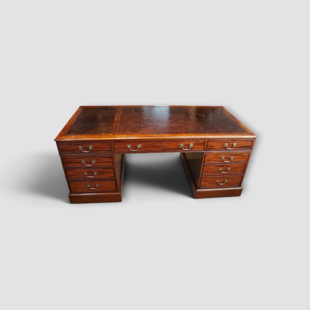 A large Victorian mahogany partners desk featuring a brown leather inset writing surface, twin drawer pedestals, brass swan-neck handles, and a wide central kneehole. View V