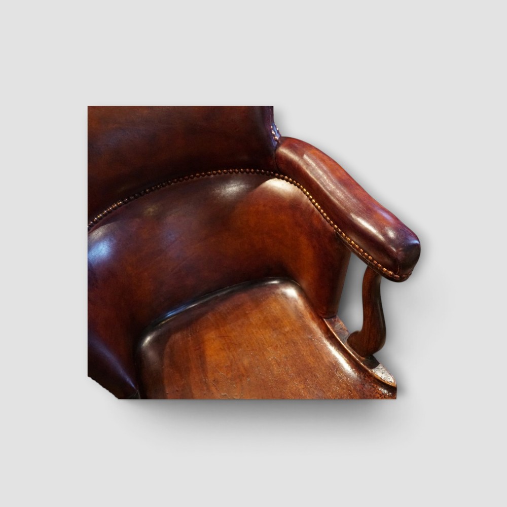 An Edwardian mahogany and chestnut brown leather swivel desk chair with a curved tub backrest, brass stud detail, and a carved four-star base. View II