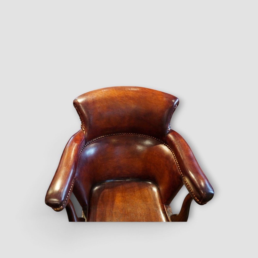 An Edwardian mahogany and chestnut brown leather swivel desk chair with a curved tub backrest, brass stud detail, and a carved four-star base. View III