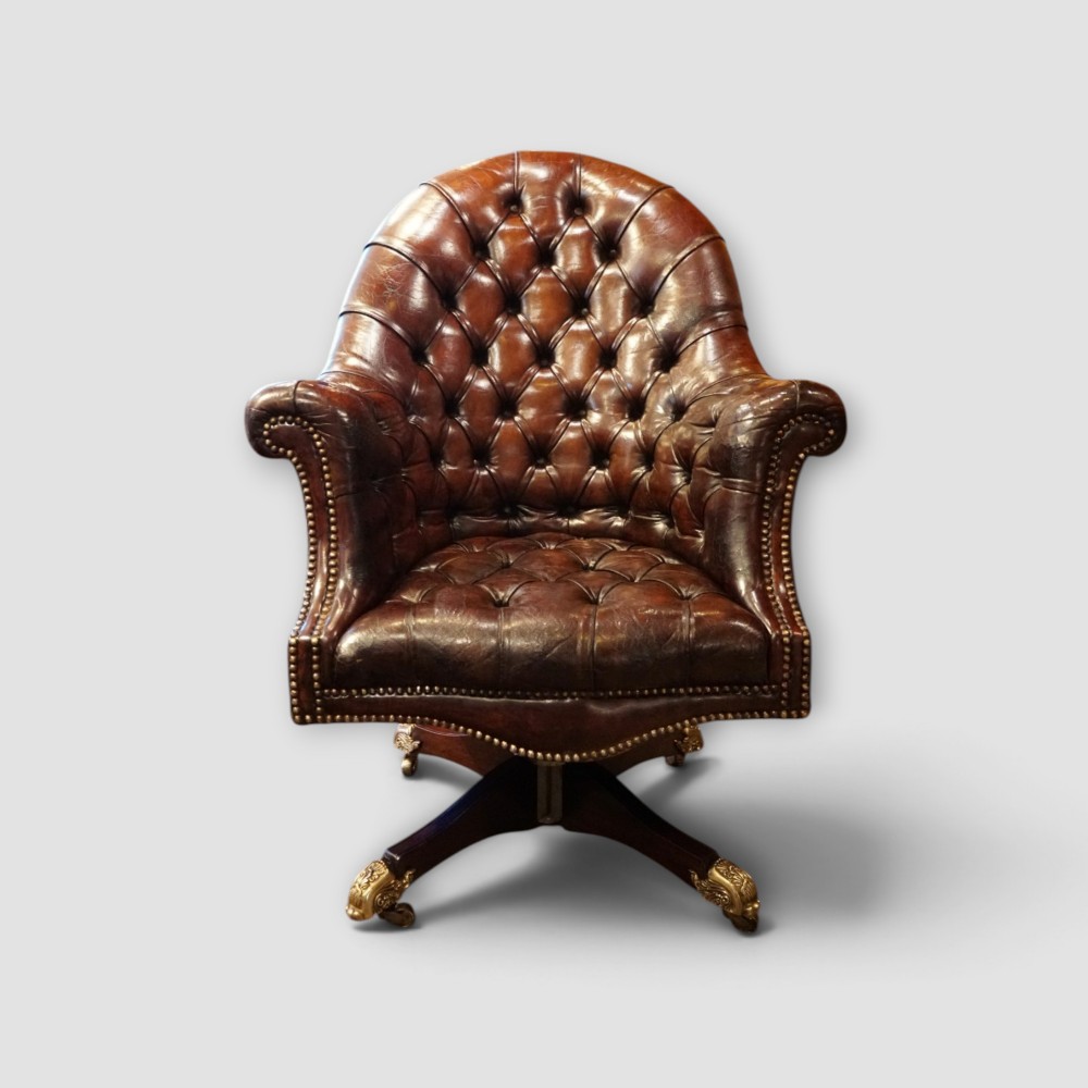 A deep buttoned brown leather captains desk chair with brass studding trim and a dark mahogany swivel base on castors.