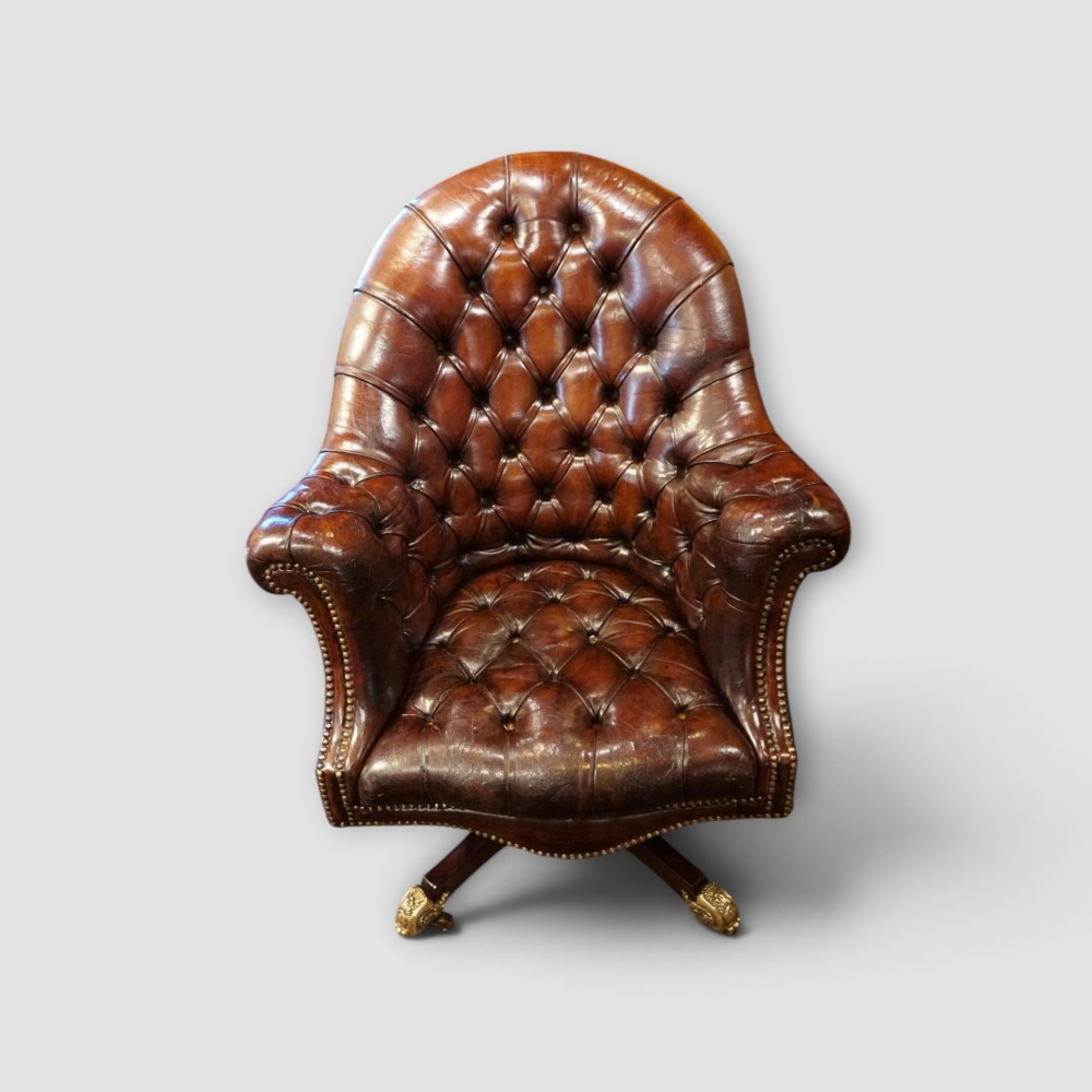 A deep buttoned brown leather captains desk chair with brass studding trim and a dark mahogany swivel base on castors. View V