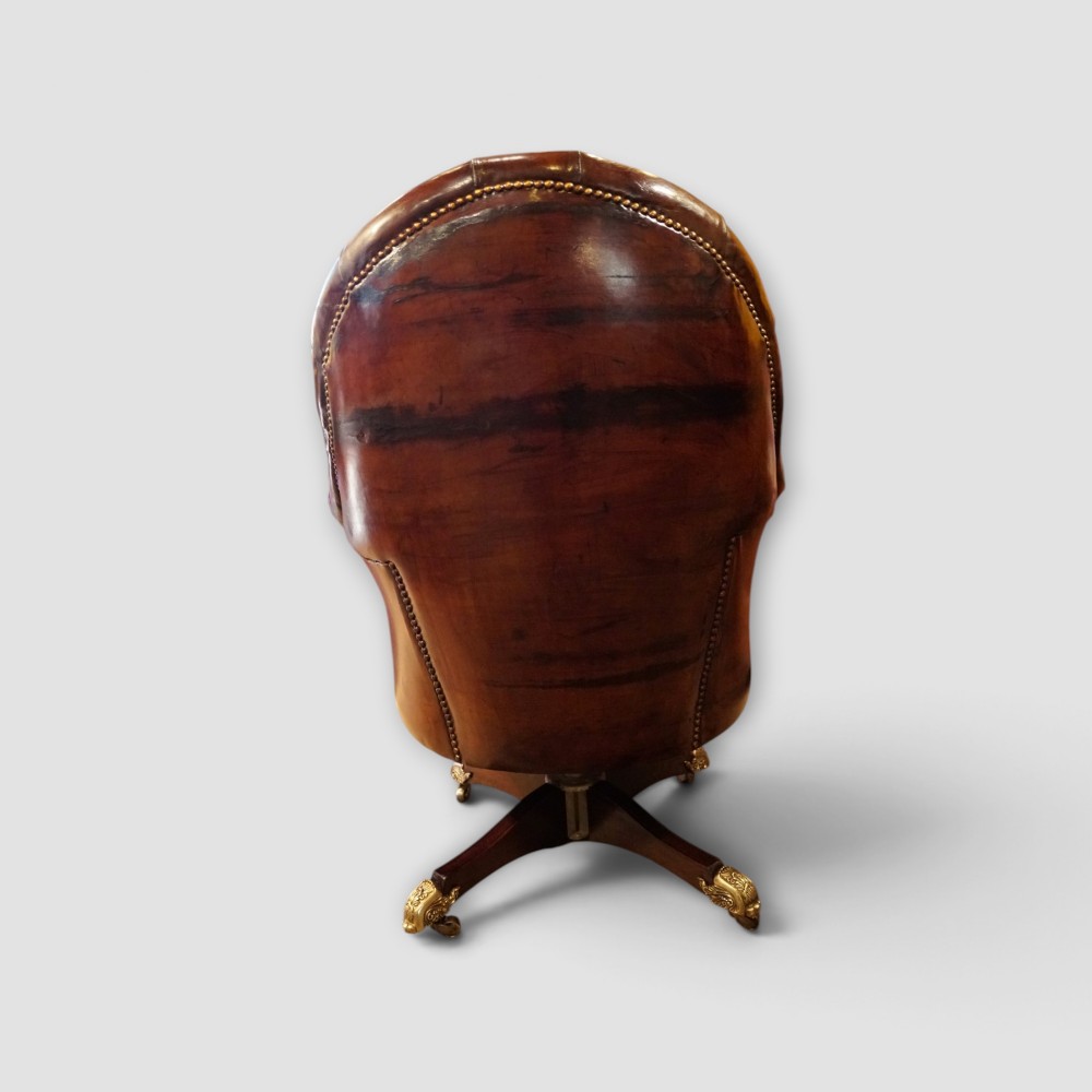 A deep buttoned brown leather captains desk chair with brass studding trim and a dark mahogany swivel base on castors. View VII
