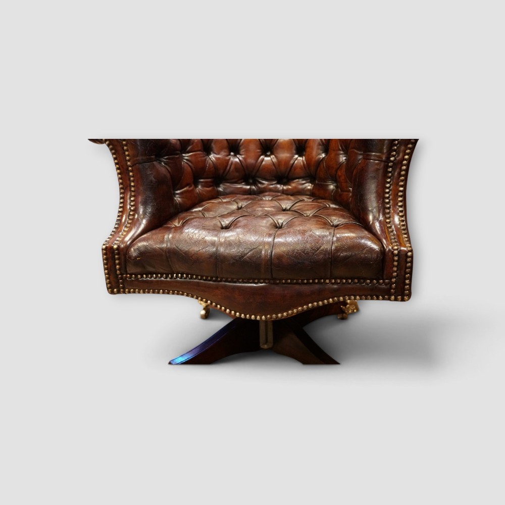 A deep buttoned brown leather captains desk chair with brass studding trim and a dark mahogany swivel base on castors. View VIII