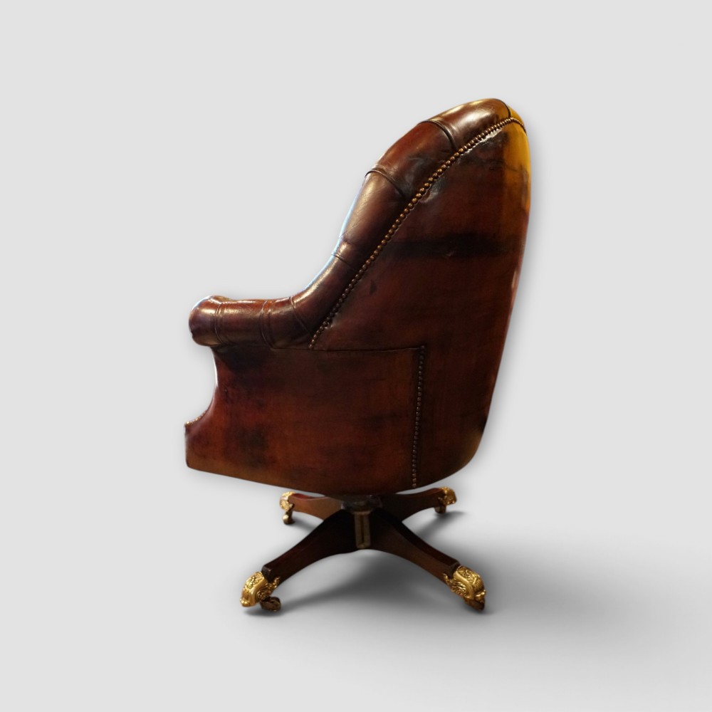 A deep buttoned brown leather captains desk chair with brass studding trim and a dark mahogany swivel base on castors. View X