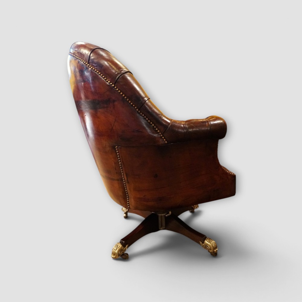 A deep buttoned brown leather captains desk chair with brass studding trim and a dark mahogany swivel base on castors. View XI
