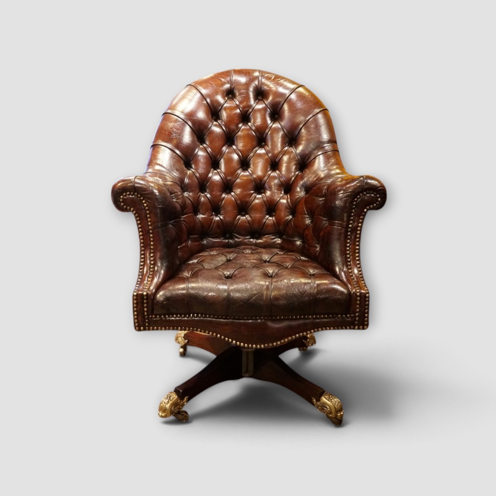 A deep buttoned brown leather captains desk chair with brass studding trim and a dark mahogany swivel base on castors. View XII
