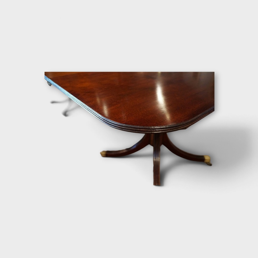 A Georgian style dark mahogany dining table featuring an extendable top, twin turned pedestal pillars, and splayed quadruped legs with brass toe caps. View IX