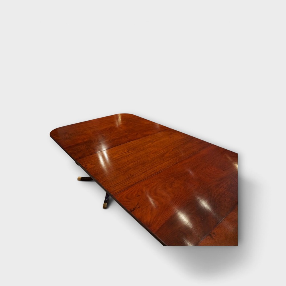 A Georgian style dark mahogany dining table featuring an extendable top, twin turned pedestal pillars, and splayed quadruped legs with brass toe caps. View X