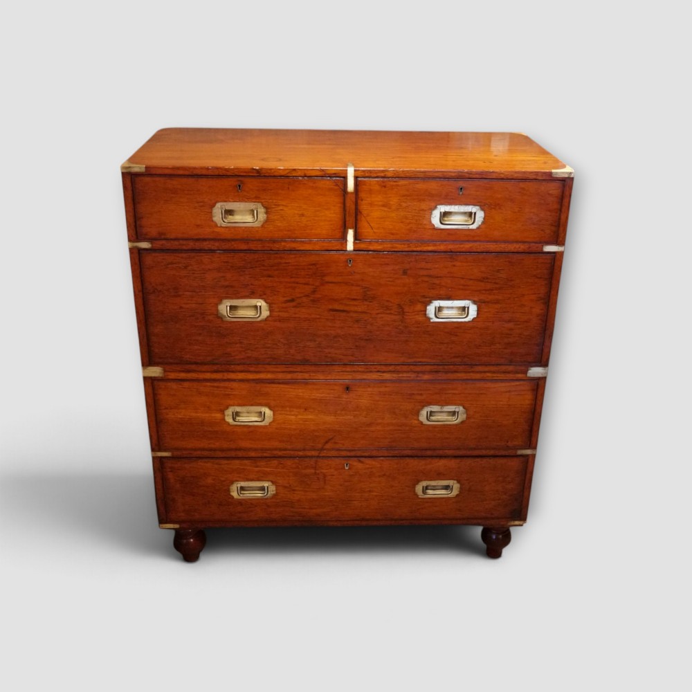 A Victorian teak two-part military campaign chest of drawers featuring flush brass handles, brass corner mounts, and turned feet.