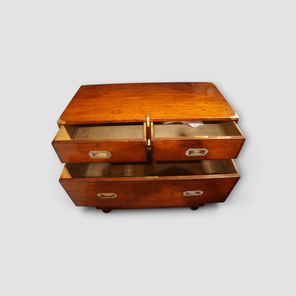 A Victorian teak two-part military campaign chest of drawers featuring flush brass handles, brass corner mounts, and turned feet. View V