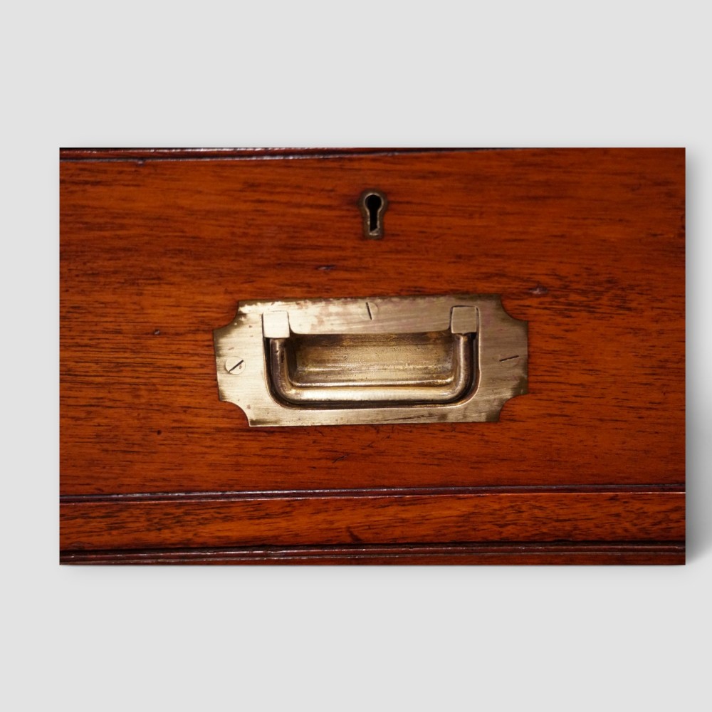 A Victorian teak two-part military campaign chest of drawers featuring flush brass handles, brass corner mounts, and turned feet. View VI