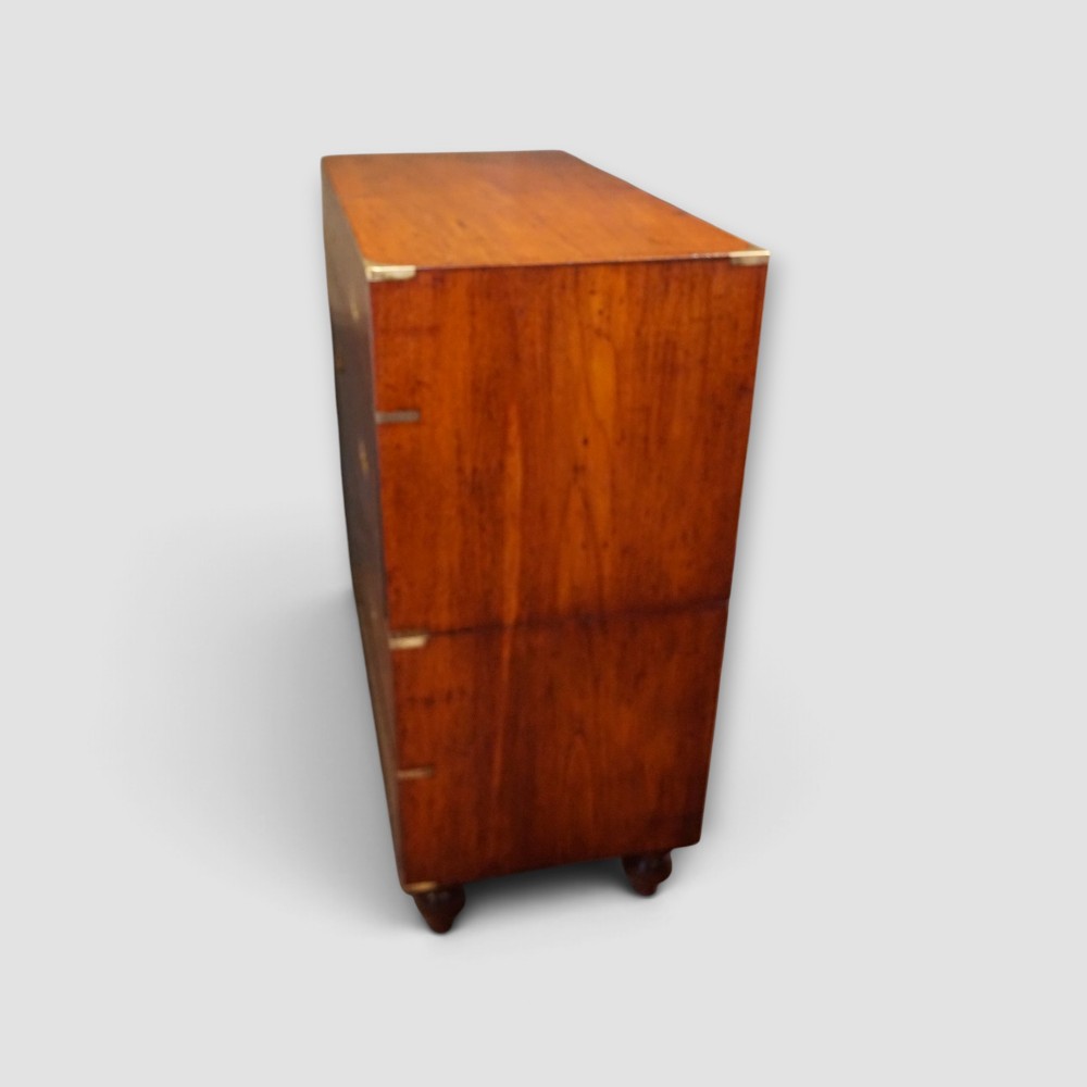 A Victorian teak two-part military campaign chest of drawers featuring flush brass handles, brass corner mounts, and turned feet. View XI
