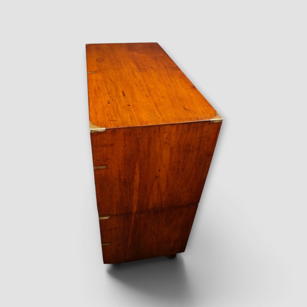 A Victorian teak two-part military campaign chest of drawers featuring flush brass handles, brass corner mounts, and turned feet. View XII