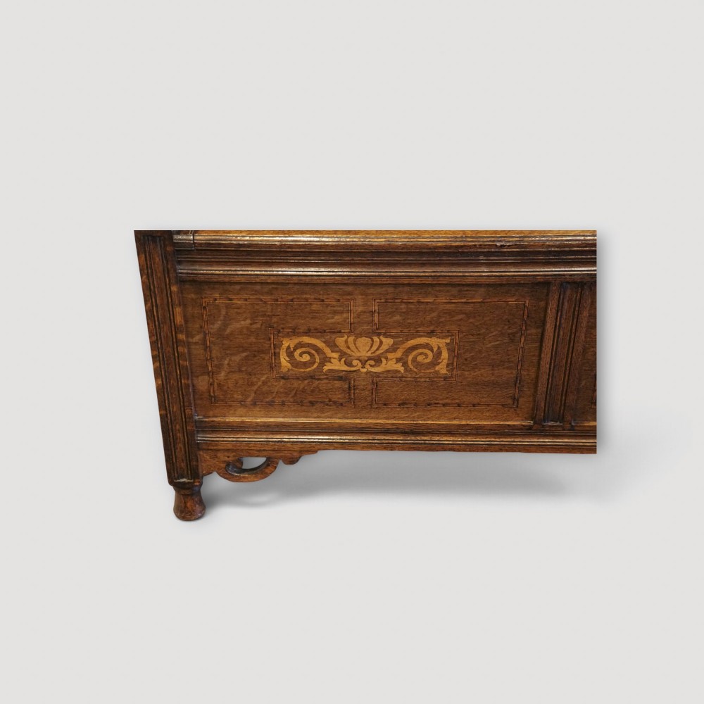 An Art Nouveau solid oak settle featuring decorative marquetry inlay across the backrest and lower front panels, curved armrests, and a lift-up storage seat. View V