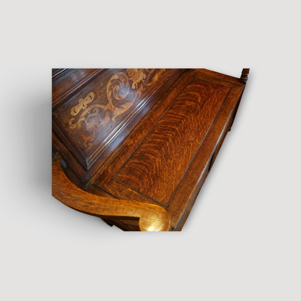 An Art Nouveau solid oak settle featuring decorative marquetry inlay across the backrest and lower front panels, curved armrests, and a lift-up storage seat. View VIII