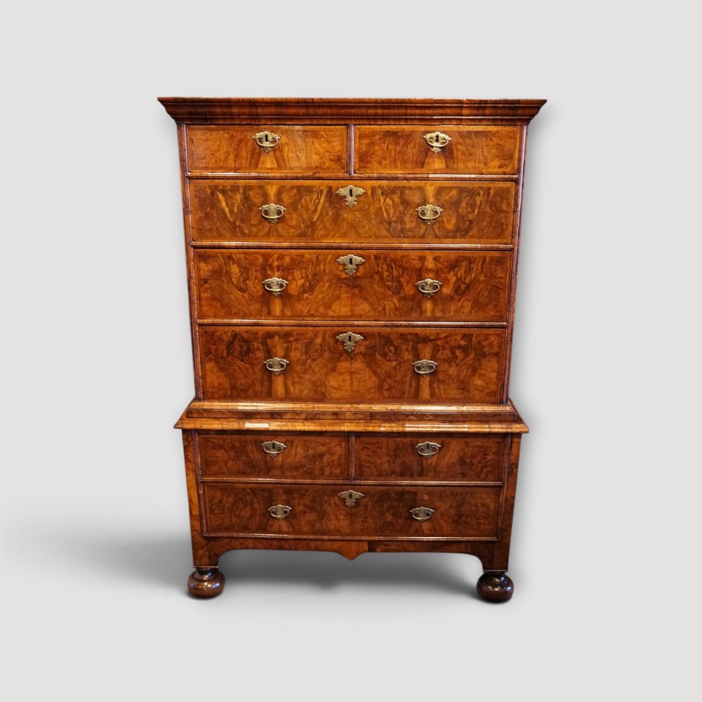 An antique Queen Anne walnut chest-on-chest in two sections featuring a multi-drawer configuration, figured grain patterns, brass drop handles, and bun feet. View VII