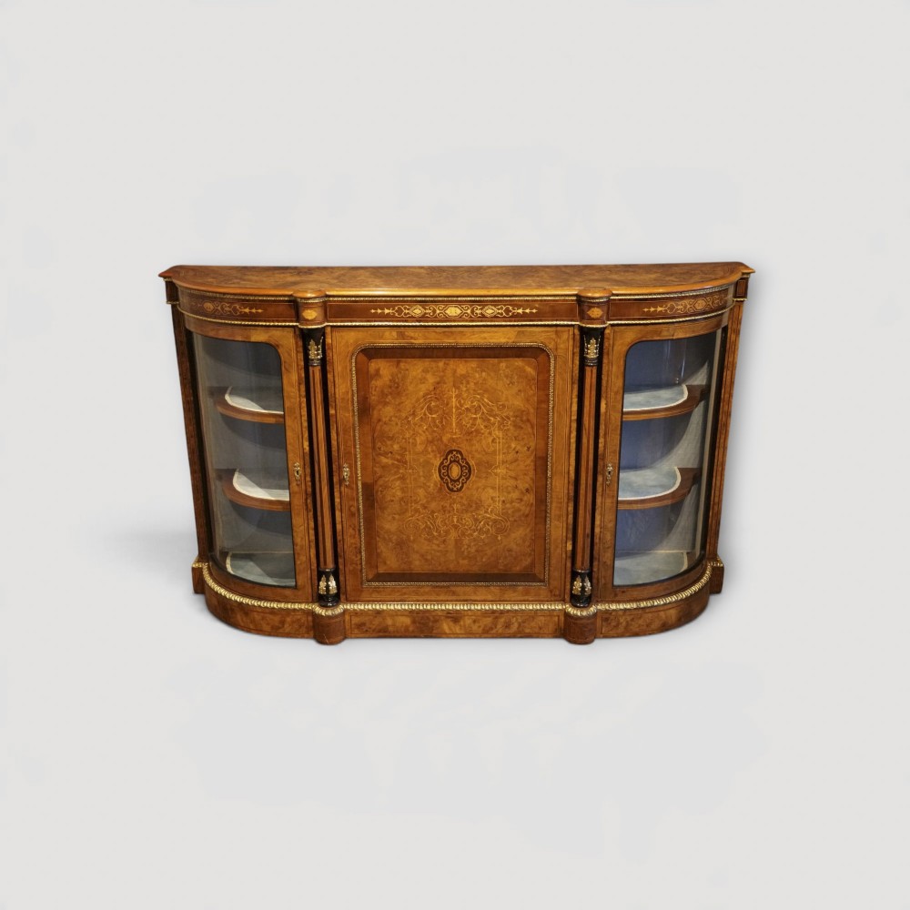 A Victorian burr walnut credenza featuring a central marquetry inlaid door flanked by two curved glazed display side cabinets with gilt mounts.