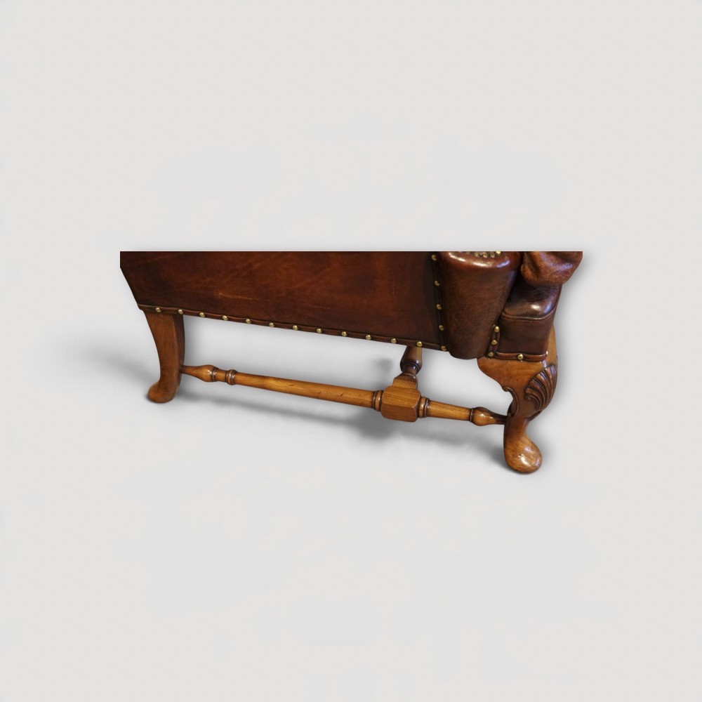 A pair of brown leather Queen Anne style wingback armchairs featuring deep seat cushions, brass stud detailing, and carved walnut cabriole legs. View IX