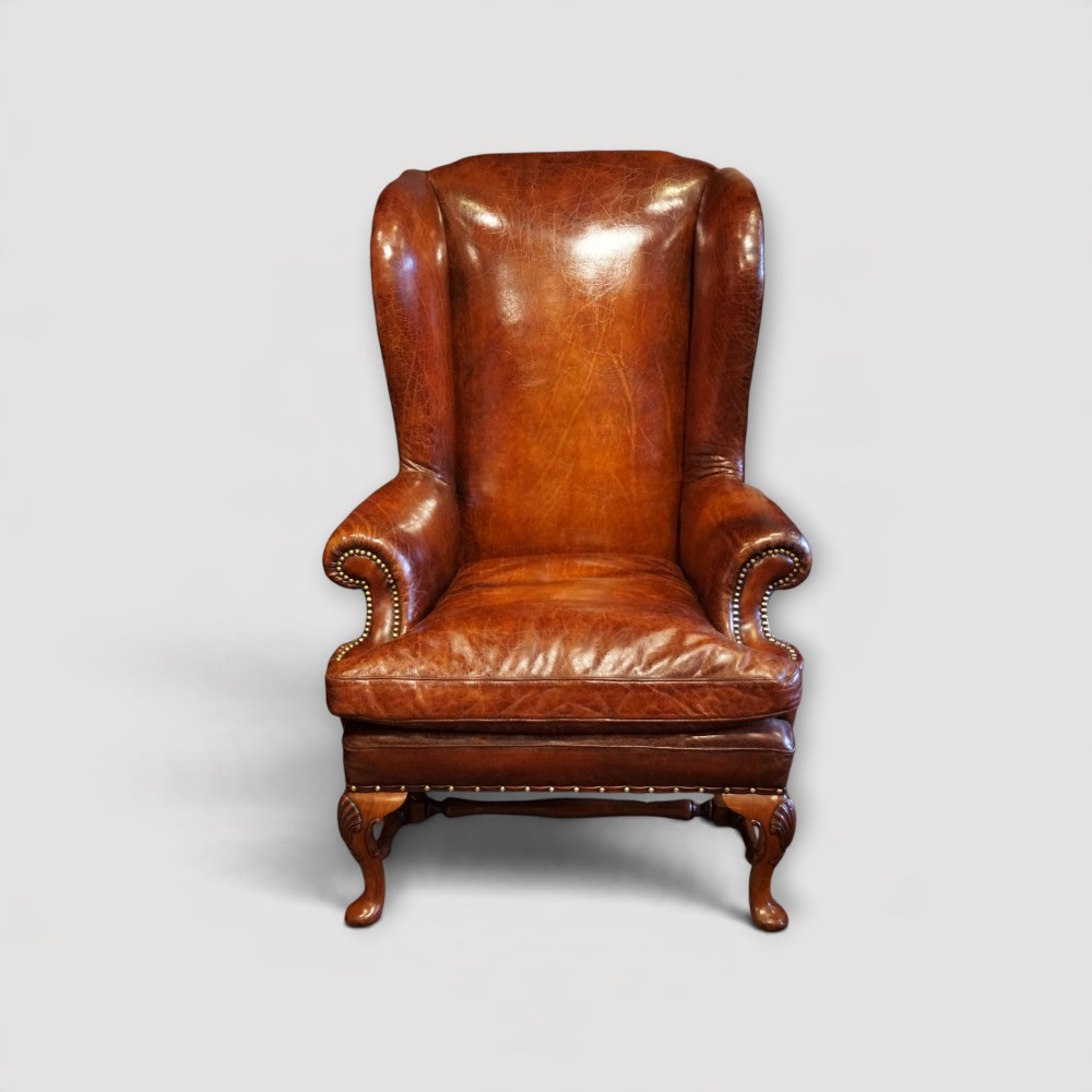 A pair of brown leather Queen Anne style wingback armchairs featuring deep seat cushions, brass stud detailing, and carved walnut cabriole legs. View XI