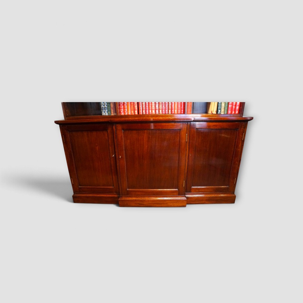An Edwardian mahogany breakfront bookcase featuring an open upper shelving section filled with books and an enclosed lower cupboard base. View III