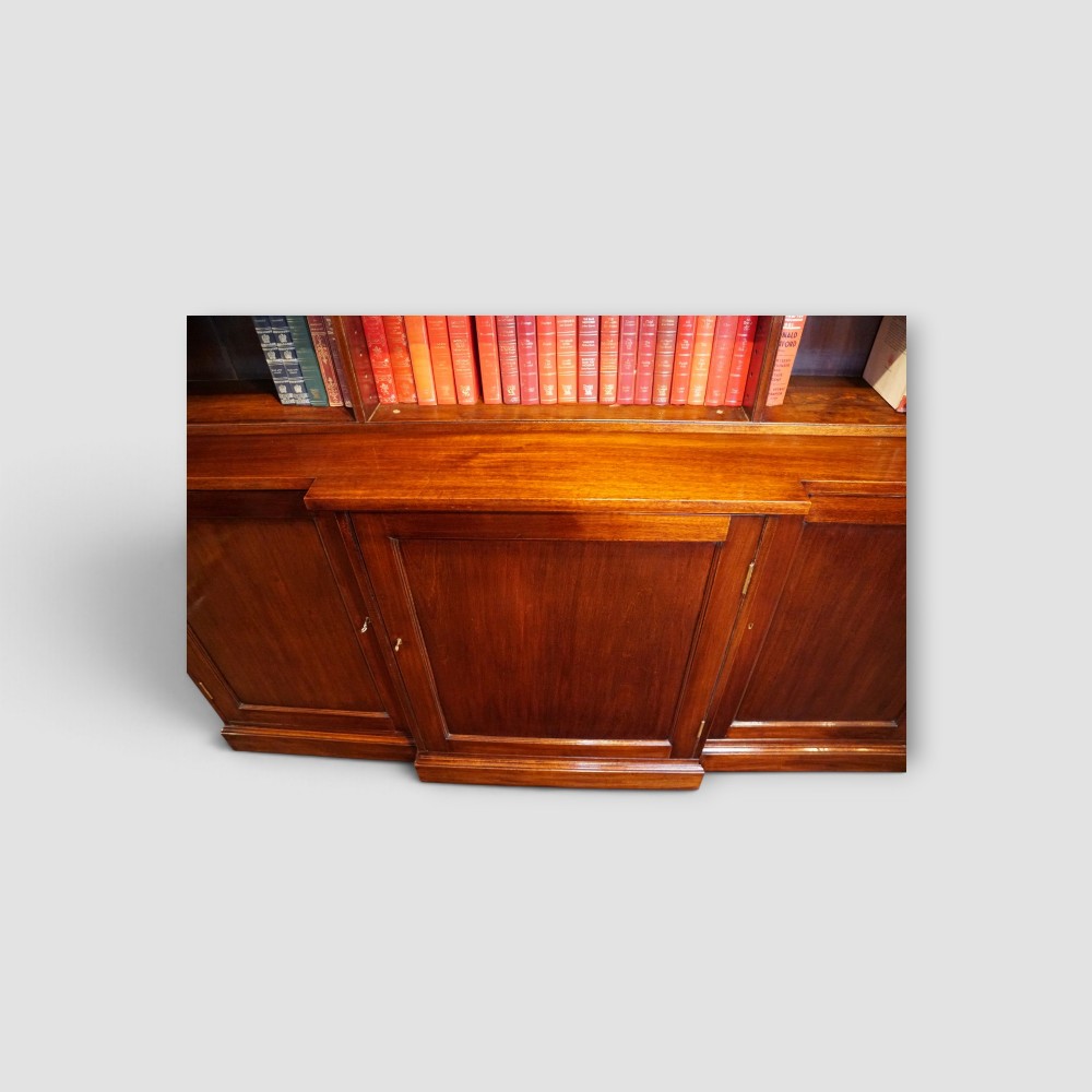 An Edwardian mahogany breakfront bookcase featuring an open upper shelving section filled with books and an enclosed lower cupboard base. View IV