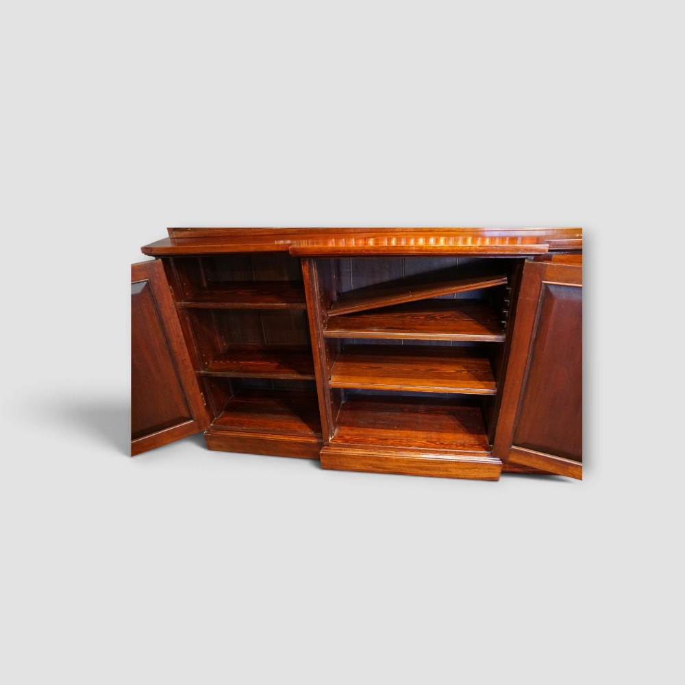 An Edwardian mahogany breakfront bookcase featuring an open upper shelving section filled with books and an enclosed lower cupboard base. View X