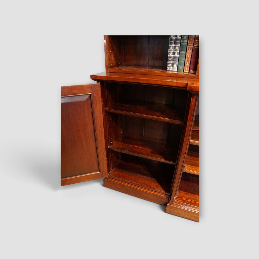 An Edwardian mahogany breakfront bookcase featuring an open upper shelving section filled with books and an enclosed lower cupboard base. View XI