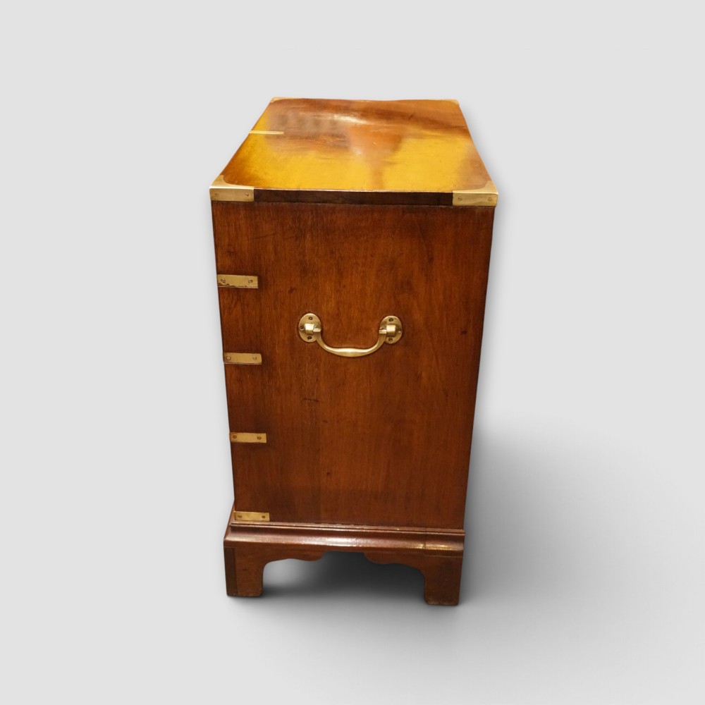 A wooden chest of drawers featuring brass corner brackets, flush handles, and two short drawers above three long drawers. View V