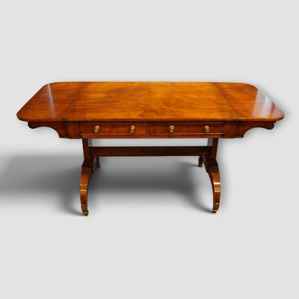 A Regency burr satinwood sofa table with drop leaves, two frieze drawers, brass handles, and splayed legs on castors.