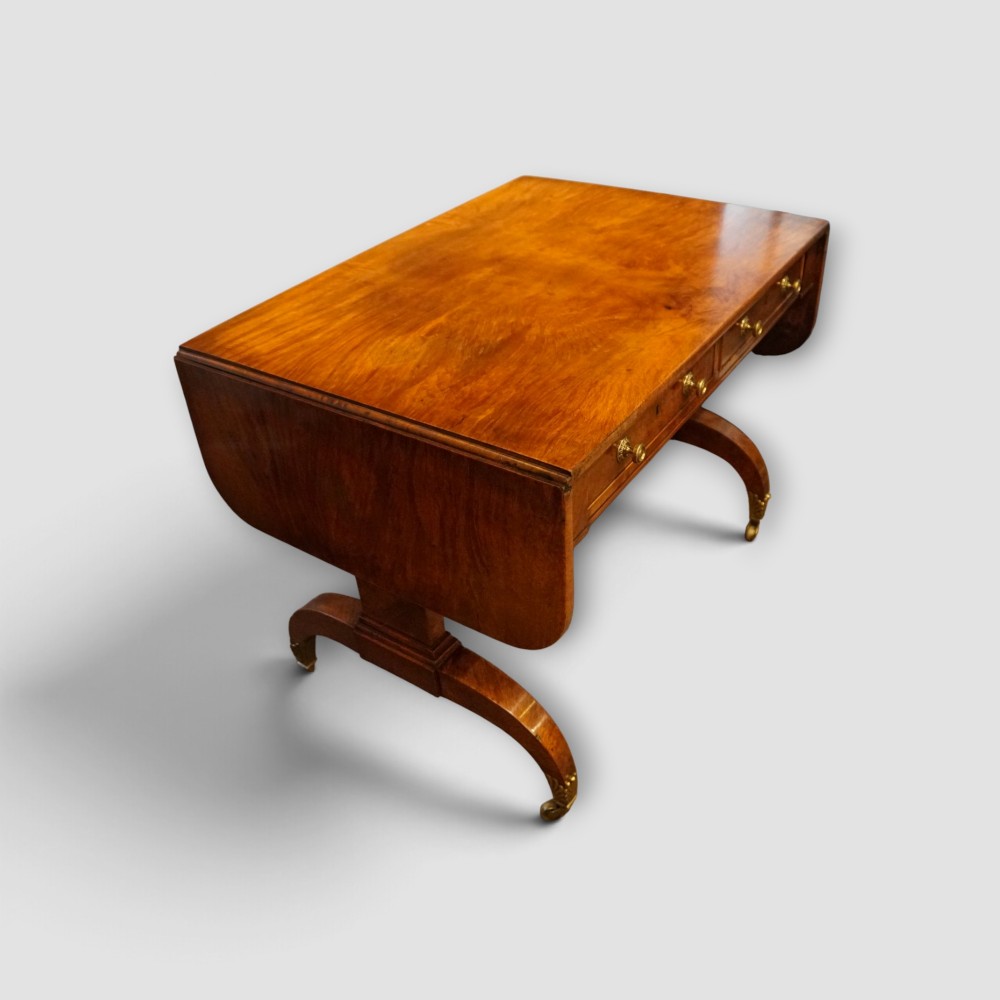 A Regency burr satinwood sofa table with drop leaves, two frieze drawers, brass handles, and splayed legs on castors. View II