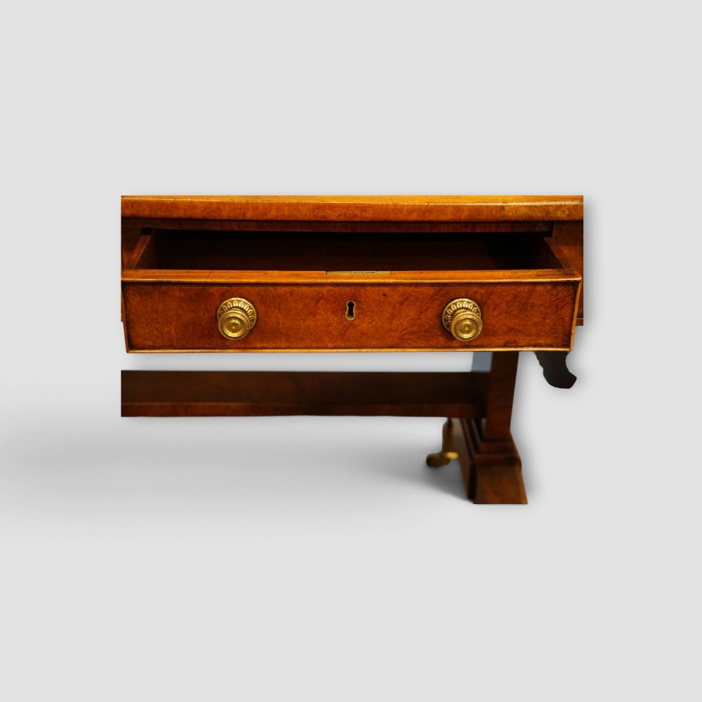 A Regency burr satinwood sofa table with drop leaves, two frieze drawers, brass handles, and splayed legs on castors. View IV